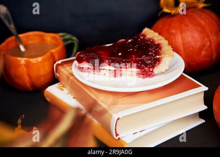 Aesthetics cozy home - autumn cup of coffee in shape of pumpkin, cherry pie and books. Atmospheric cozy coffee time. Stock Photo