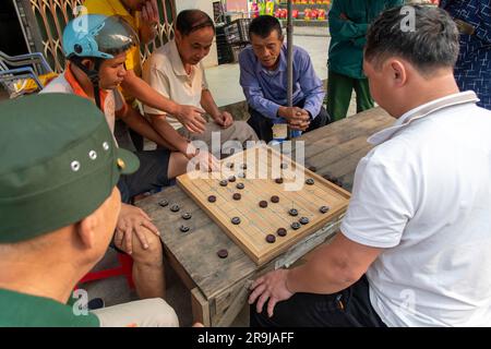 Bac Ha, Vietnam-April 2023; High angle view of two men playing Xiangqi, also called Chinese chess or elephant chess while being watched by several oth Stock Photo