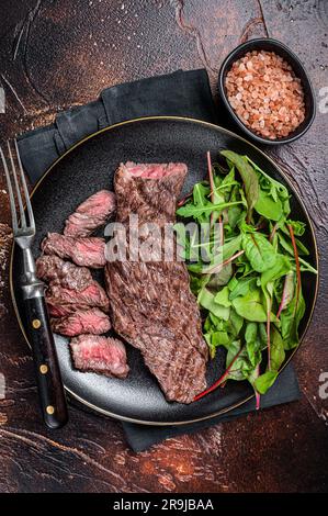 Juicy Grilled Machete skirt beef meat steak on plate with salad. Dark background. Top view. Stock Photo