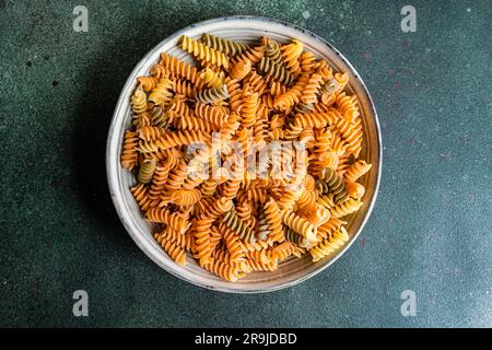 Top view of raw uncooked fusilli pasta made from wheat, beetroot and spinach in the bowl on dark green background Stock Photo