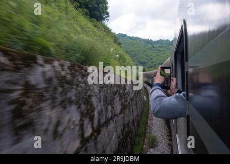 Man traveler photographing railroad from the train window using camera on his mobile phone while traveling by railway through Balkans Stock Photo