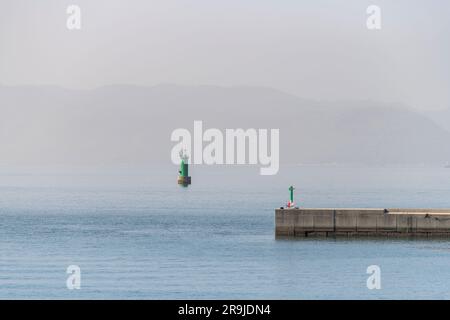 Partial view of the concrete wave barrier of Miyanoura Port on Naoshima Island, Japan with a tranquil sea, green small lighthouse in the water and bac Stock Photo