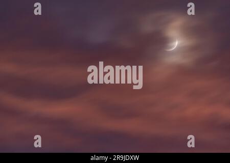 Crescent moon throught sunset clouds Stock Photo