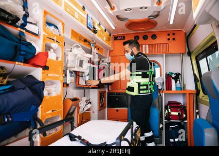 Side view of concentrated guy in uniform and medical mask checking facility in automobile while working as paramedic Stock Photo
