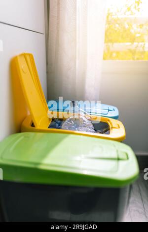 Side view of recycling containers and plastic bottle inside opened yellow recycling trash placed in kitchen near window Stock Photo