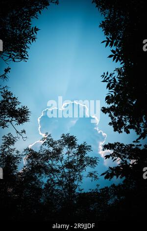 Dramatic sky with cloud and light rays, framed by trees Stock Photo