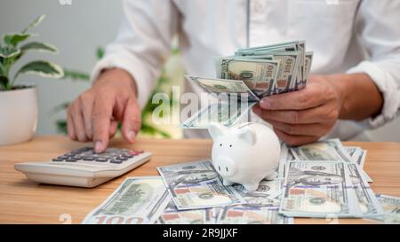 Woman counting calculator and putting coins in piggy bank close up    Businessman holding dollar bill and pressing calculator, calculate savings for f Stock Photo