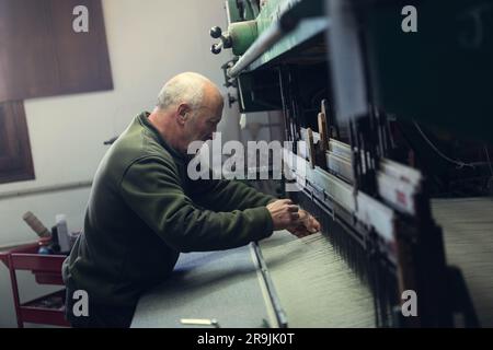Side view of concentrated senior male working standing at workbench and working in workshop with assorted professional cotton mill machine Stock Photo