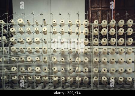 Rows of white thread hanging on metal stand in cotton mill factory workshop against windows and wall with no people Stock Photo