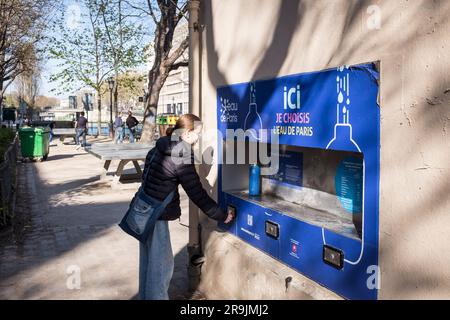 A young caucasian girl fills her reusable bottle at an eau de paris sparkling water public fountain in a park in Paris, on a beautiful sunny spring day. Stock Photo