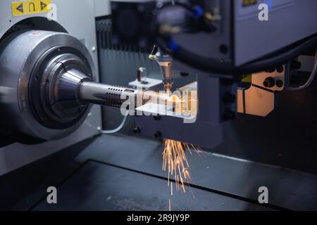 An industrial worker in protective gear operating a robotic machine cutting through a large metallic object, emitting sparks in the process Stock Photo