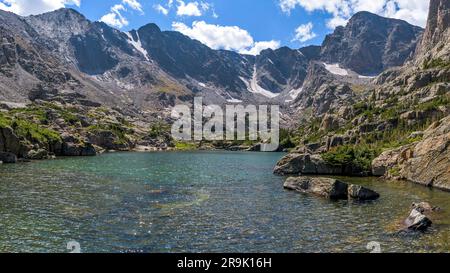 Lake of Glass - A panorama of clear and colorful Lake of Glass surrounded by rugged high peaks of Continental Divide on a sunny Summer day. RMNP, CO. Stock Photo