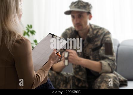 Psychologist making notes during therapy session with sad male soldier, PTSD Stock Photo