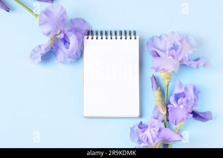 Notebook with clean page with purple flowers irises on orange background. Flat lay style. Stock Photo