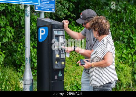 People paying for parking in a car park at a pay and display ticket machine. Paying to park, buying parking ticket. In England, UK. Stock Photo