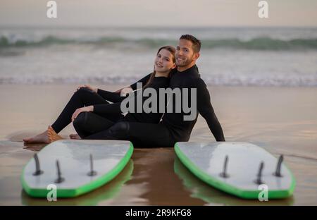 Romantic Young Couple Wearing Wetsuits Posing With Surfboards On The Beach Stock Photo