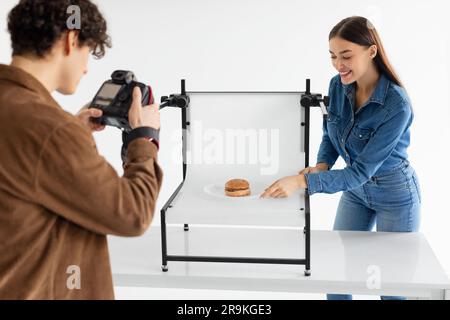 Male photographer and his female assistant doing content photoshoot for fast food restaurant, taking photos of burger Stock Photo