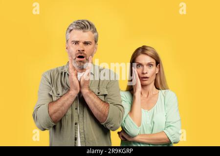 Shocked european middle aged husband and wife with open mouth looking at camera, posing on yellow background Stock Photo
