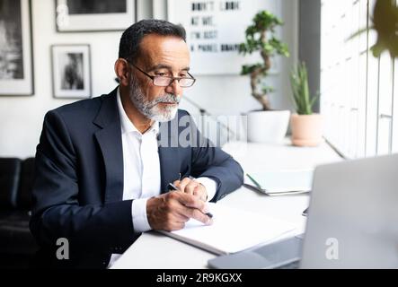 Serious mature european businessman in suit work on laptop, making notes, watch webinar Stock Photo