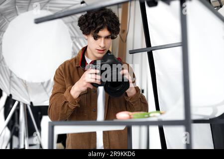 Young man photographer taking professional photos of various desserts in photostudio, using digital camera Stock Photo