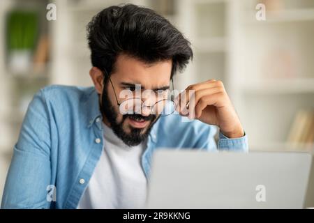 Shocked Indian Freelancer Guy Taking Off Glasses And Looking At Laptop Screen Stock Photo