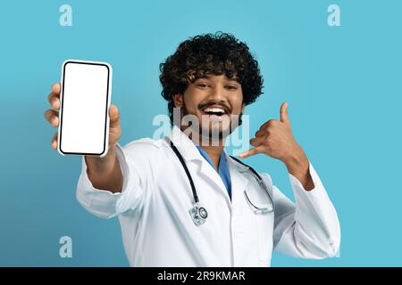 Positive handsome young indian doc showing phone with mockup Stock Photo