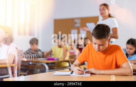 Focused preteen schoolboy writing in workbook during lesson Stock Photo