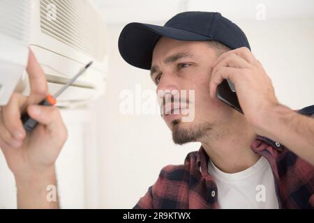 young handyman repairing air conditioning system calling for help Stock Photo