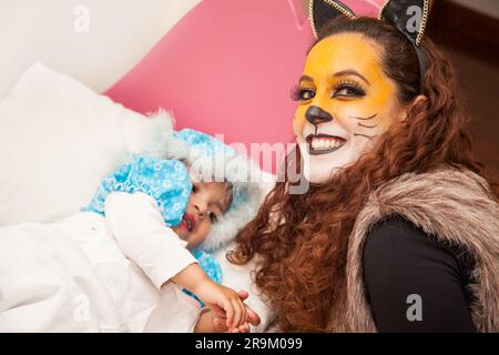 Mother playing wolf character and little girl playing grandma. Real family having fun while using costumes of the Little red riding hood tale in Hallo Stock Photo