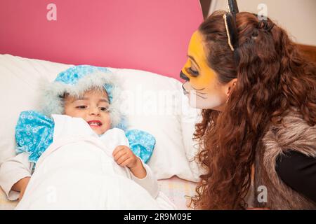 Little girl playing grandma character and mother playing wolf. Real family having fun while using costumes of the Little red riding hood tale in Hallo Stock Photo