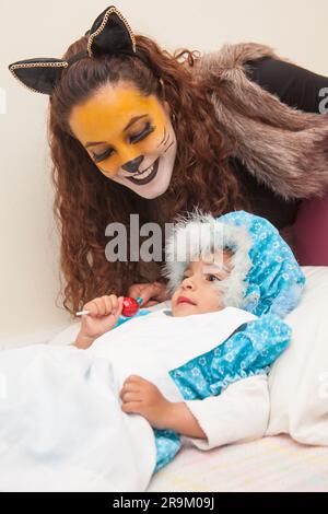 Little girl playing grandma character and mother playing wolf. Real family having fun while using costumes of the Little red riding hood tale in Hallo Stock Photo