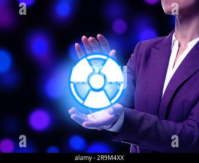 Woman holding glowing radiation warning symbol on dark background with blue and purple blurred lights, closeup Stock Photo