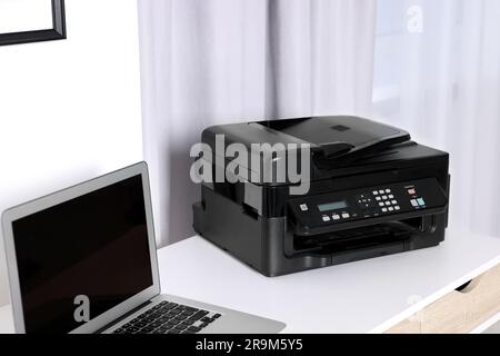 Modern printer with paper near laptop on white desk at home Stock Photo