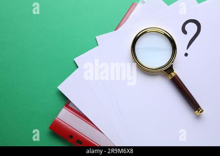 Magnifying glass, folder with paper sheets and question mark on green background, top view Stock Photo