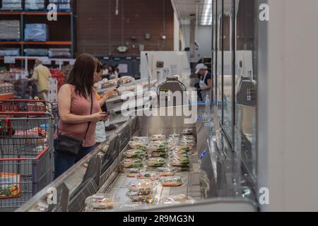 A vibrant image captures a bustling scene at a Costco food court. Customers are seen patiently waiting, eagerly anticipating their turn to try the newly introduced sushi. The excitement in the air is palpable as people gather around the food counter. Costco, the renowned wholesale retailer, has taken a bold step by adding sushi to its famously affordable food court menu. The introduction of this new cuisine has resulted in long lines and increased wait times, as eager members rush to sample Costco's latest offering.Customers wasted no time in sharing their opinions online, resulting in a flurr Stock Photo