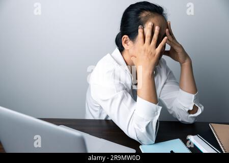 A business office worker is an asian woman is sitting in front of the laptop computer. A businesswoman stressing her body part fingers, hands arm. A f Stock Photo