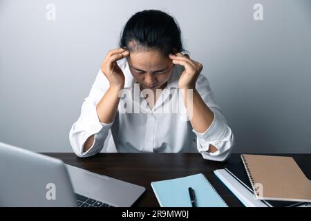 A business office worker is an asian woman is sitting in front of the laptop computer. A businesswoman stressing her body part fingers, hands arm. A f Stock Photo