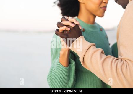 Midsection of happy african american couple holding hands and dancing on beach Stock Photo