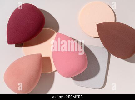 Multiple egg-shaped makeup sponges placed on a beige background. View from above. Stock Photo