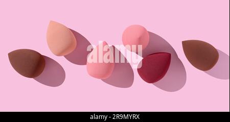 Multiple egg-shaped makeup sponges placed on a pink background. View from above. Stock Photo