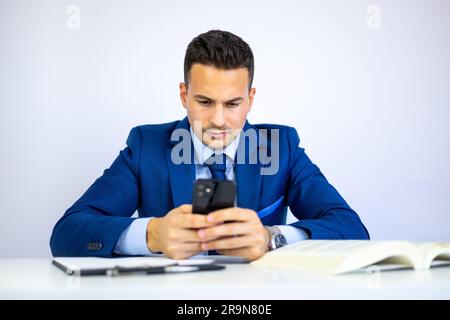 Handsome businessman, economist, lawyer, manager or executive director typing with a smartphone and checking financial documents at the office desk. Stock Photo