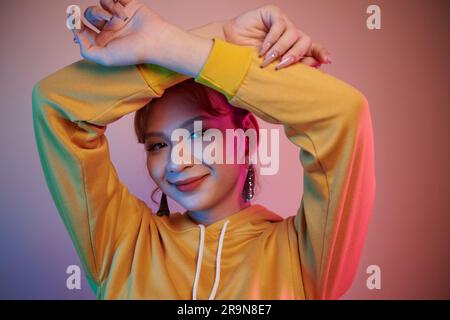Portrait of joyful young transgender woman in holding standing in neon light and looking at camera Stock Photo