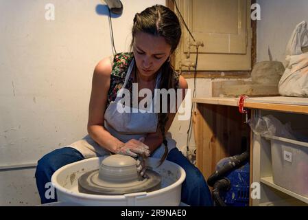 young ceramist woman hands working and shaping clay on the lathe or potter's wheel inside a pottery workshop Stock Photo