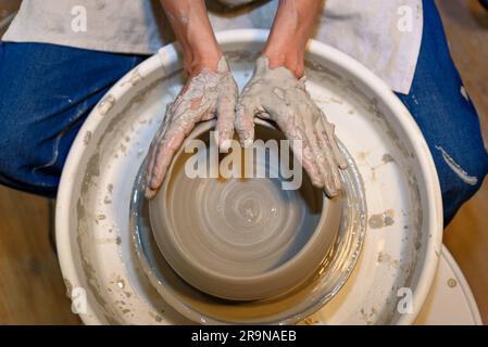 close up of ceramist woman hands working and shaping clay on the lathe or potter's wheel inside a pottery workshop Stock Photo