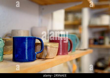 Close up of set of colorful handmade ceramic mugs on a wooden table inside a ceramic and pottery shop. Warm natural light Stock Photo