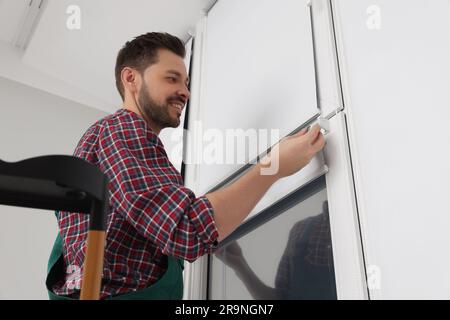 Worker in uniform installing roller window blind indoors Stock Photo