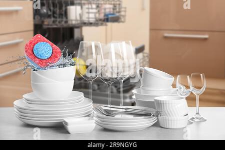 Many clean tableware in kitchen. Dishwasher detergent falling into bowl with water Stock Photo