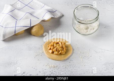A round flat piece of rolled out dough stuffed with apples and cinnamon on a light gray table. Cooking delicious mini pies with apples, Stock Photo