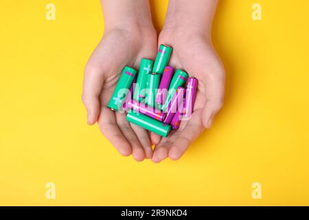 Woman holding many different batteries on yellow background, top view Stock Photo