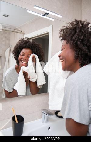 Happy african young woman drying the face skin with a towel in bathroom. Stock Photo